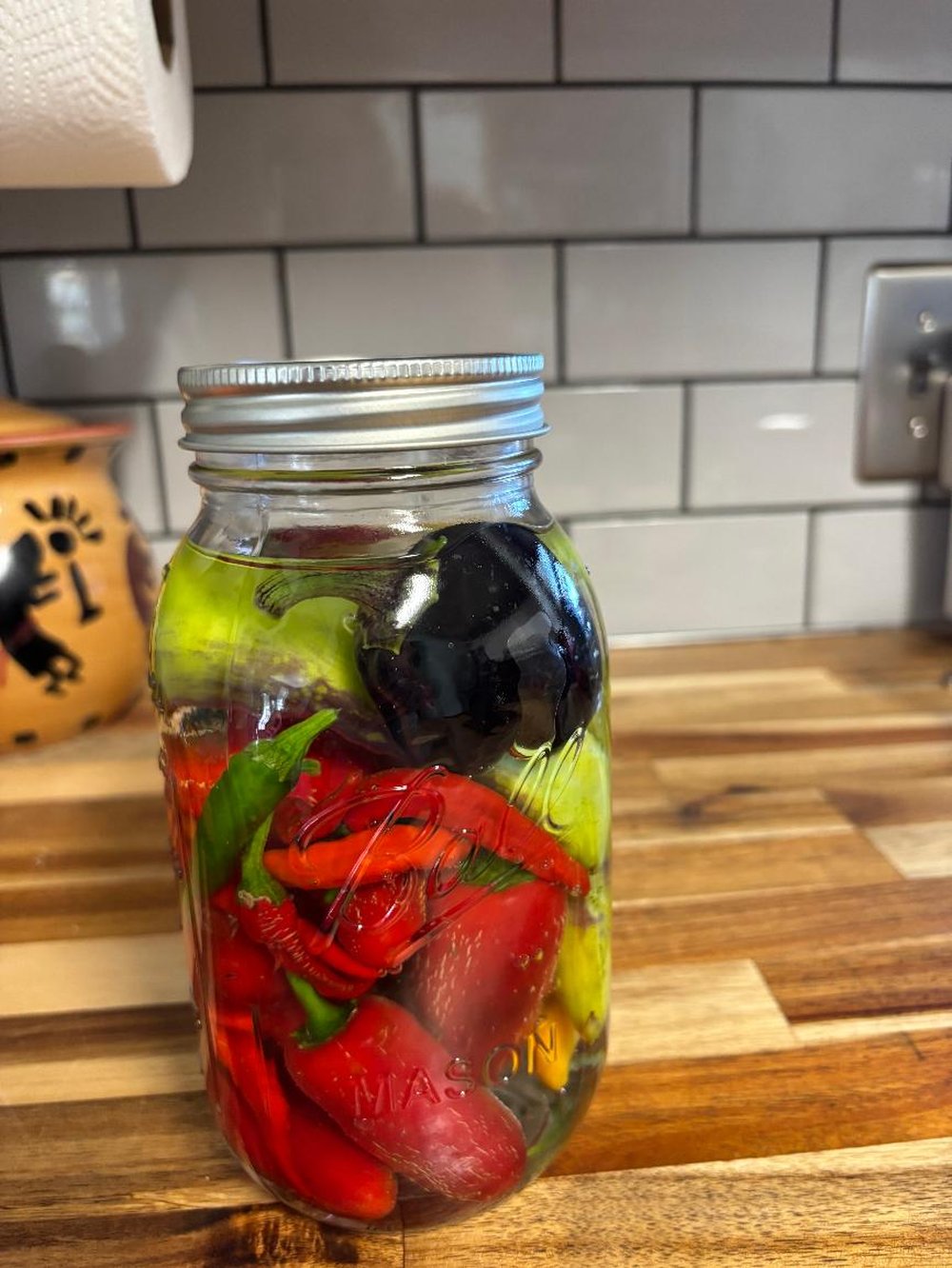 A jar of pickled peppers backlit like stained glass, red and green peppers glowing